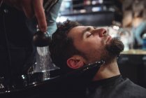 Homem relaxante ao receber lavagem de cabelo na barbearia — Fotografia de Stock
