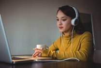 Woman listening to headphones while using laptop in study room at home — Stock Photo