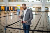 Бізнесмен тримає посадковий талон і перевіряє свій мобільний телефон в терміналі аеропорту — стокове фото