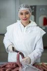 Fleischereifachverkäuferin schneidet Wurst mit Messer in Fleischfabrik — Stockfoto