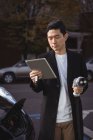 Uomo che utilizza tablet digitale mentre tiene il caricabatterie per auto presso la stazione di ricarica del veicolo elettrico — Foto stock