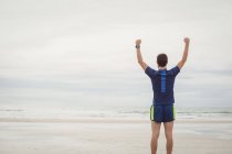 Вид сзади спортсмена, стоящего на пляже с поднятыми руками — стоковое фото