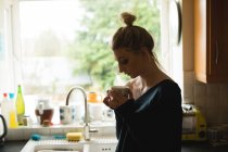 Donna premurosa che tiene una tazza di caffè in cucina a casa — Foto stock