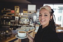 Portrait of waitress standing with cup of coffee in cafe — Stock Photo