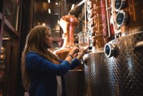 Mujer sosteniendo un vaso de medir en fábrica de cerveza - foto de stock