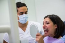 Dentista segurando espelho na frente do paciente na clínica — Fotografia de Stock