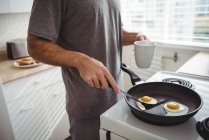 Milieu de l'homme avec tasse à café en utilisant une spatule pour la cuisson des œufs frits — Photo de stock