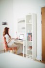 Mujer embarazada usando el ordenador portátil en la sala de estudio en casa - foto de stock