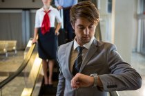 Geschäftsmann kontrolliert Zeit, während er die Rolltreppe am Flughafen hinuntersteigt — Stockfoto