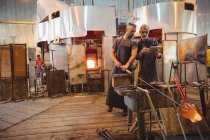 Team of glassblowers using digital while working over a molten glass at glassblowing factory — Stock Photo