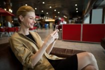 Femme d'affaires utilisant un téléphone portable dans la salle d'attente au terminal de l'aéroport — Photo de stock