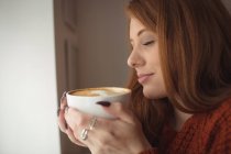 Gros plan de la belle femme tenant une tasse de café à la fenêtre — Photo de stock