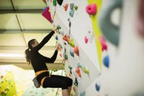 Жінка практикує скелелазіння на штучній стіні скелелазіння в спортзалі — стокове фото