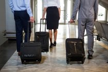 Businessmen and female staff walking with luggage in waiting area at airport — Stock Photo
