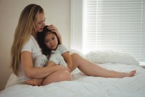 Прихильна мати обіймає свою дочку в спальні вдома — стокове фото