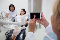 Женщина, использующая мобильный телефон в клинике с людьми в фоновом режиме — стоковое фото