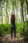 Задний вид женщины, выполняющей упражнения на растяжку в лесу — стоковое фото
