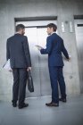 Empresários em pé por elevador e pressionando o botão no escritório — Fotografia de Stock