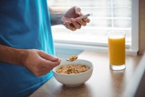Mid-section of man using mobile phone while having breakfast in kitchen at home — Stock Photo