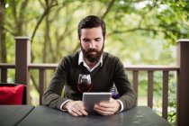 Людина використовує цифровий планшет, маючи келих вина в барі — стокове фото
