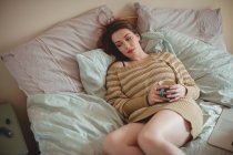 Продумана жінка тримає чашку кави і лежить на ліжку вдома — стокове фото