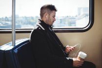 Geschäftsmann hält eine Einweg-Kaffeetasse in der Hand und hört im Zug Musik per Handy — Stockfoto