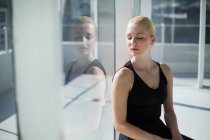 Балерина сидит у стеклянного окна в студии — стоковое фото