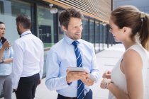 Businessman and colleague discussing over digital tablet outside office building — Stock Photo