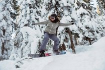 Female snowboarder jumping over the slope on snow covered mountain — Stock Photo