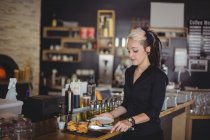Cameriera che serve muffin in un piatto al bancone in caffè — Foto stock