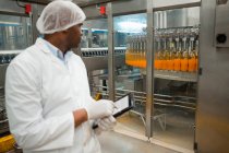 Operaio maschio con tablet digitale mentre ispeziona le bottiglie di succo in fabbrica — Foto stock