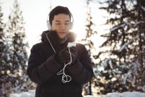 Человек слушает музыку в наушниках со смартфона зимой — стоковое фото