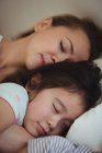 Madre e hija durmiendo juntas en el dormitorio en casa - foto de stock