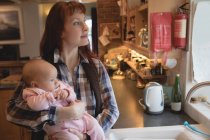 Nachdenkliche Mutter trägt Baby zu Hause in der Küche — Stockfoto