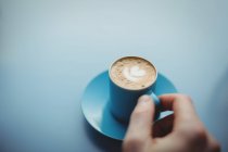 Mano tenendo tazza di caffè su sfondo blu — Foto stock