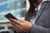 Середній розділ обміну повідомленнями бізнес-леді на мобільному телефоні, стоячи на міській вулиці — стокове фото