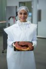 Portrait of female butcher holding tray of meat at meat factory — Stock Photo