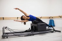 Mujer ejercitándose en equipos de reformador en el gimnasio - foto de stock