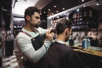 Парикмахер мужчина стрижет волосы клиента триммером в парикмахерской — стоковое фото