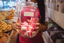 Seção intermediária do comerciante feminino segurando jarro de doces turcos no balcão na loja — Fotografia de Stock