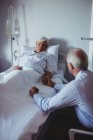 Ill mulher dormindo na cama enquanto homem preocupado sentado ao lado de sua cama no hospital — Fotografia de Stock