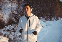 Чоловік слухає музику в навушниках під час бігу по засніженому шляху взимку — стокове фото