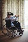Homme âgé assis sur fauteuil roulant et utilisant casque de réalité virtuelle dans la chambre à coucher à la maison — Photo de stock