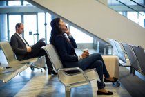 Жінка-комісарка з чашкою кави розмовляє на мобільному телефоні в зоні очікування в терміналі аеропорту — стокове фото
