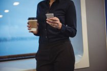 Meados de seção de empresária com xícara de café usando telefone enquanto estava de pé no trem — Fotografia de Stock