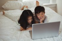 Frères et sœurs utilisant un ordinateur portable dans la chambre à coucher à la maison — Photo de stock