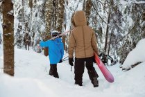 Vista trasera de pareja con esquí y snowboard caminando sobre ladera nevada - foto de stock