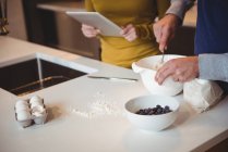 Paar nutzt digitales Tablet beim Zubereiten von Plätzchen in der heimischen Küche — Stockfoto