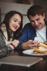 Casal usando telefone celular enquanto toma café da manhã em casa — Fotografia de Stock