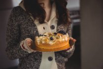 Mid section of woman holding blueberry cake in living room at home — Stock Photo